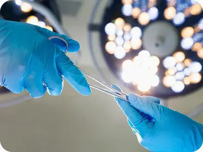 Surgeons exchanging surgical tool under bright lights.
