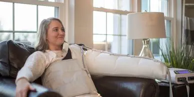 Woman using arm compression therapy device.