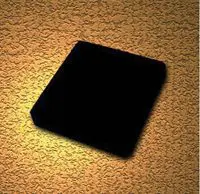 Black square-shaped object on a textured surface with warm lighting.