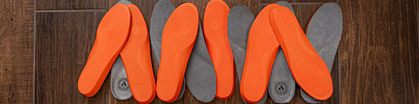 Pair of orange and gray shoe insoles on a wooden surface.